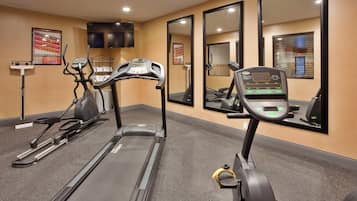 Un gimnasio con cintas de correr, bicicletas estáticas y un espejo grande.