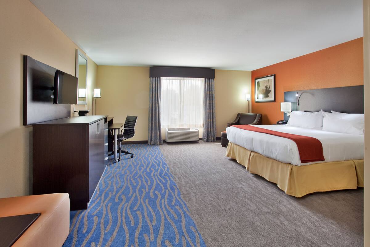 A hotel room with a bed, desk, chair, TV, and a large window with curtains.