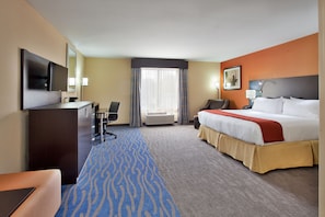 A hotel room with a bed, desk, chair, TV, and a large window with curtains.