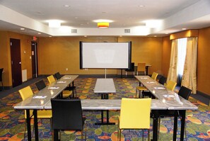 A conference room with a large projection screen, long tables, and chairs.