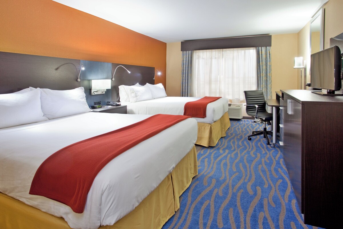 A hotel room with two beds, a desk with a computer, a chair, and a television.