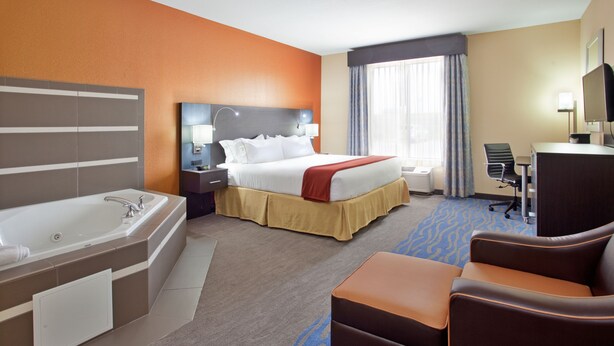 A hotel room with a large bed, a separate bathroom with a bathtub, a desk with a chair, and a large window with curtains. - Holiday Inn Express & Suites St Louis Airport by IHG (St. Louis)
