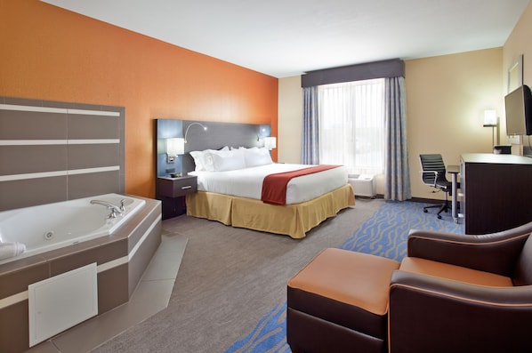 A hotel room with a large bed, a separate bathroom with a bathtub, a desk with a chair, and a large window with curtains.