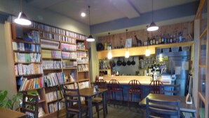 A library with bookshelves, tables, chairs, and a kitchen area with hanging pots.