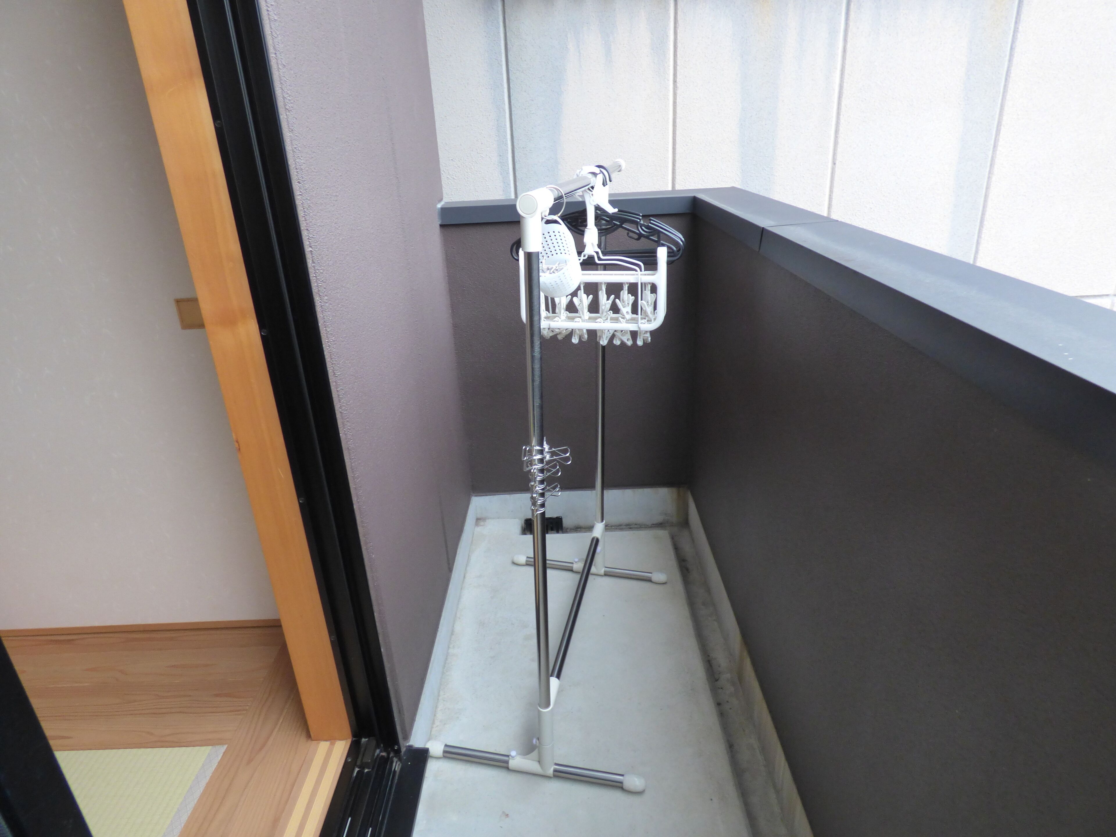 A corner of a room with a metal rack holding a white towel, a window with blinds, and a wooden floor.