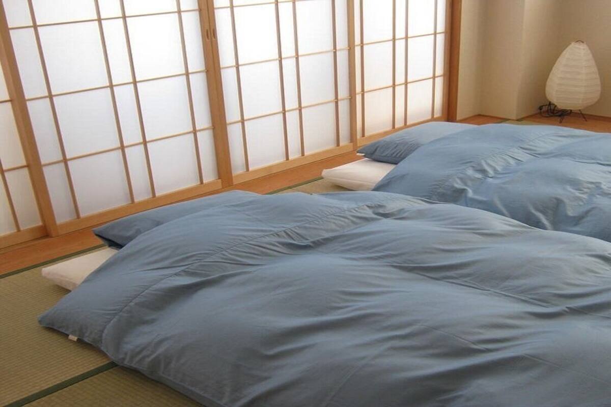 A room with tatami flooring, a shoji screen, and two beds with blue bedding.