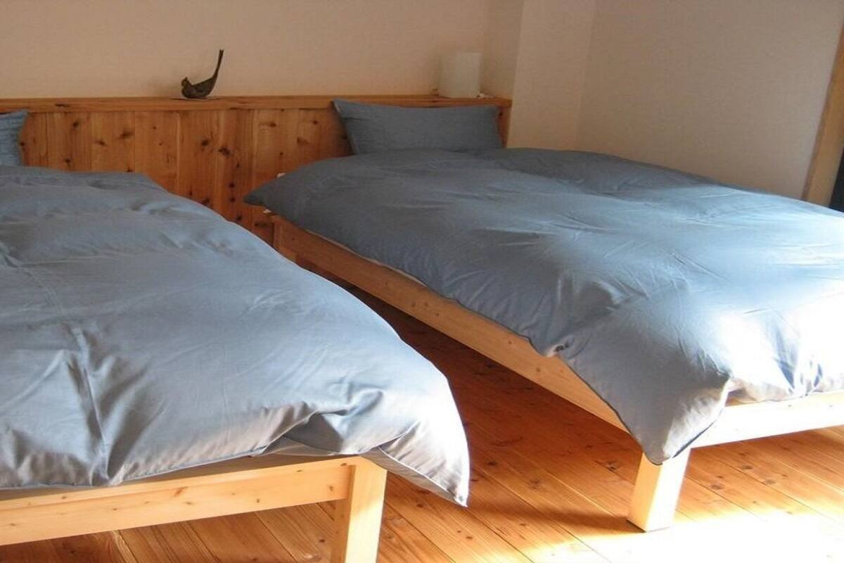 Two wooden beds with grey bedding in a room with wooden flooring and a wooden headboard.