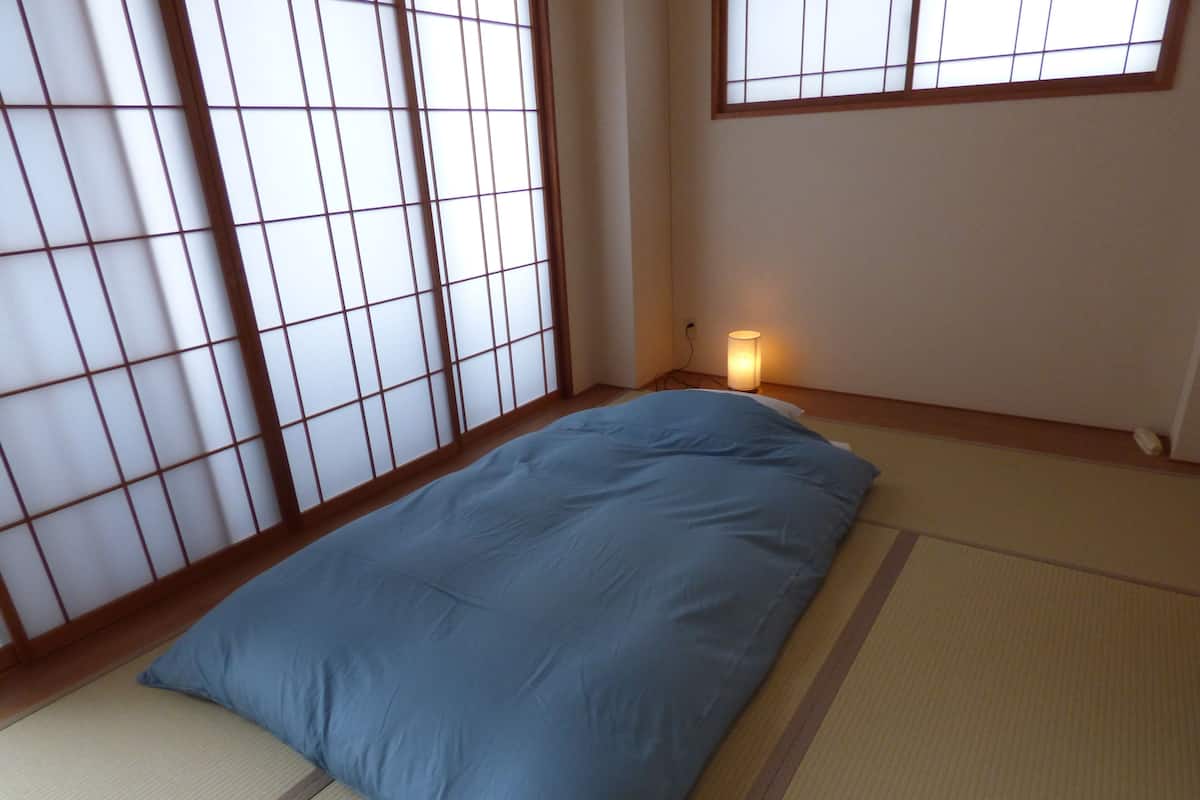 A room with tatami flooring, a blue mattress, and a shoji screen.