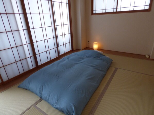 A room with tatami flooring, a blue mattress, and a shoji screen.