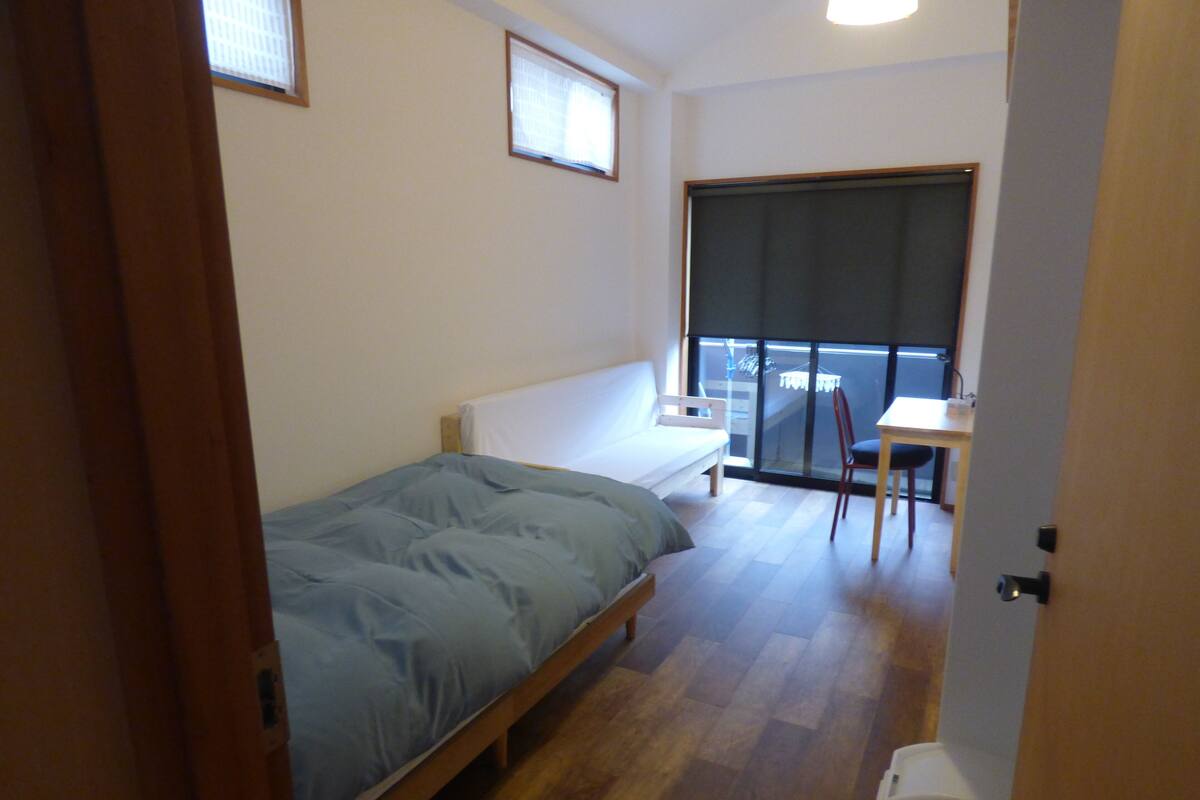 A small, single-room apartment with a bed, a desk, and a chair.