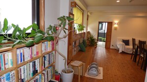 A cozy room with wooden bookshelves filled with books, a wooden floor, a small table with chairs, and a potted plant.