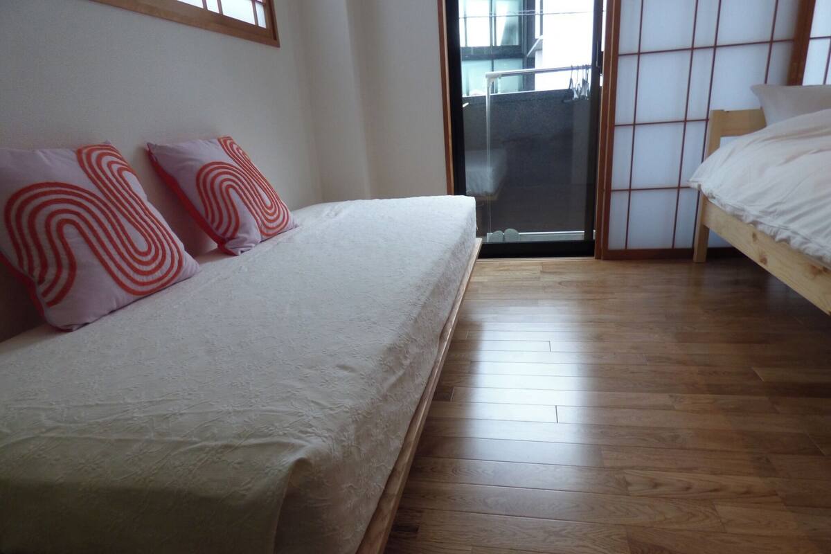 A bedroom with a bed, a wooden floor, and a sliding glass door leading to a balcony.