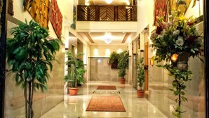 Eine geräumige Hotelhalle mit einem zentralen Kronleuchter, Zimmerpflanzen und einem roten Teppich, der zum Eingang führt.