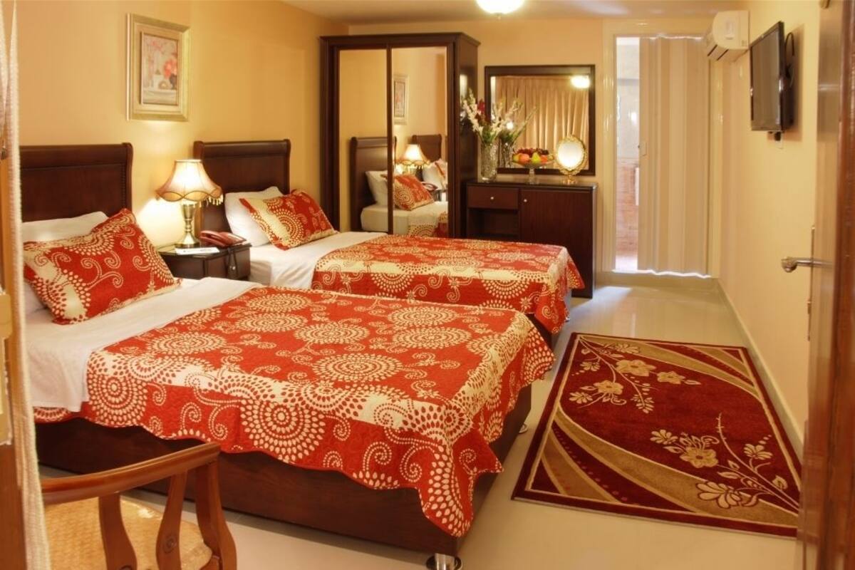 A hotel room with two beds, a desk, a mirror, and a TV.