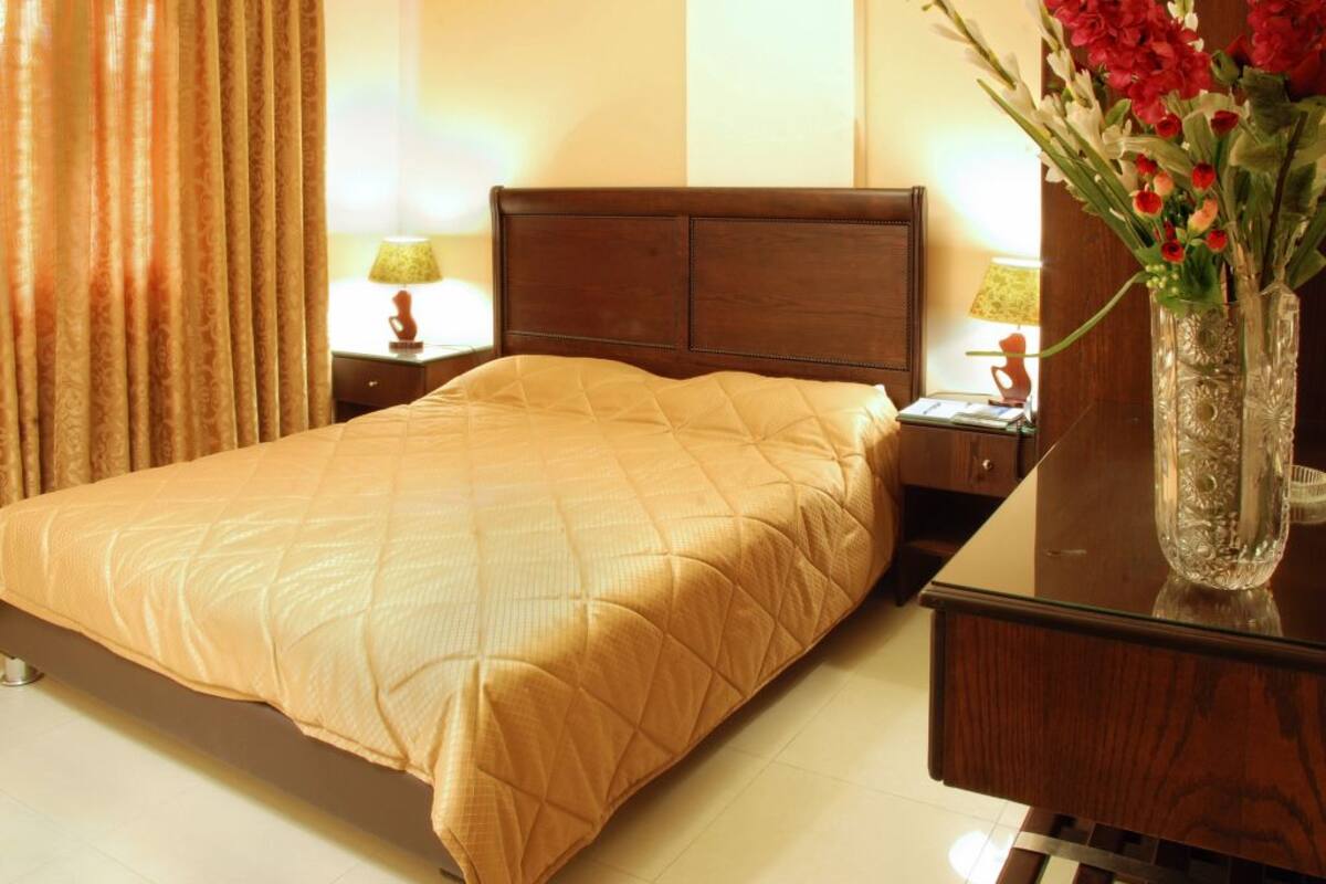 A hotel room with a bed, a nightstand, a lamp, and a vase with flowers.