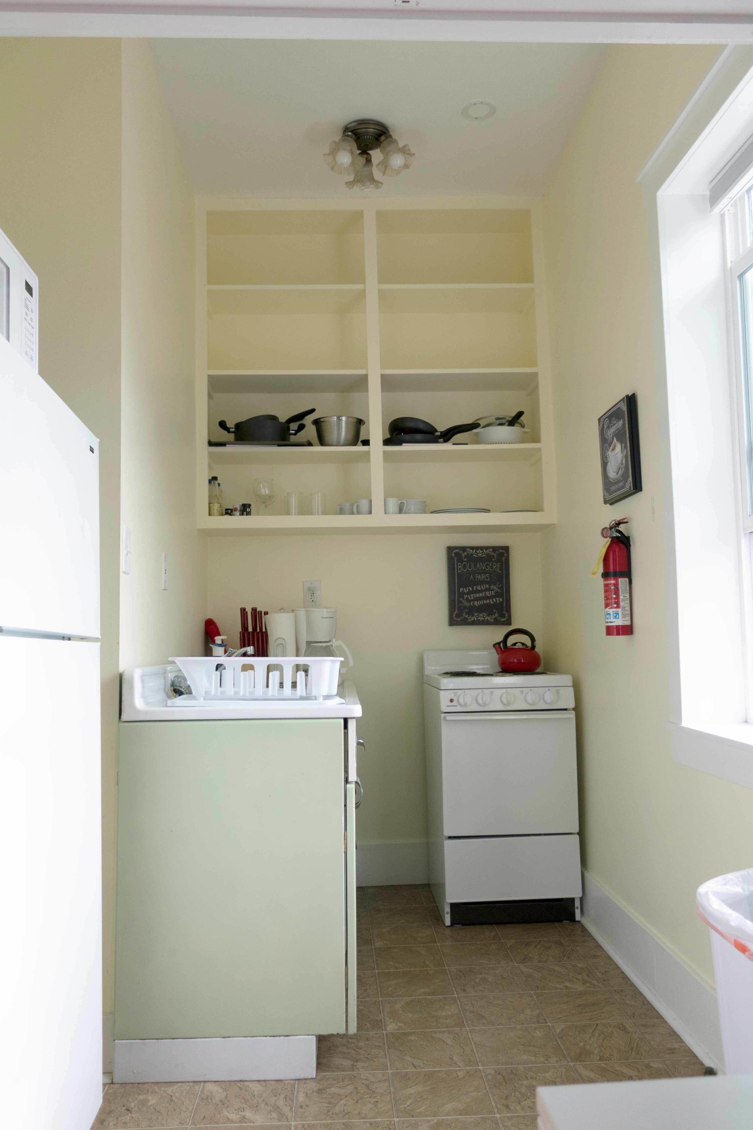 A compact kitchen with a white refrigerator, stove, and shelves above.