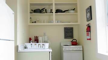 A compact kitchen with a white refrigerator, stove, and shelves above.