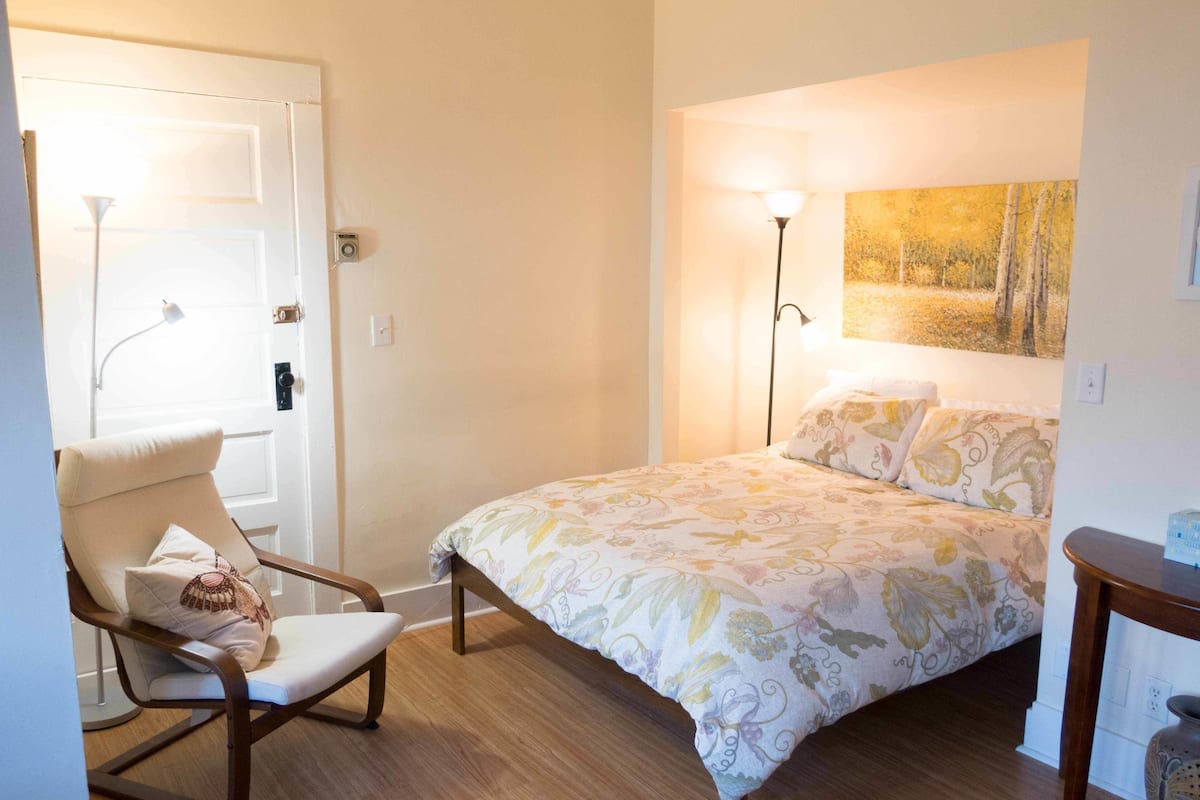 A bedroom with a bed, a chair, a painting, and a lamp.