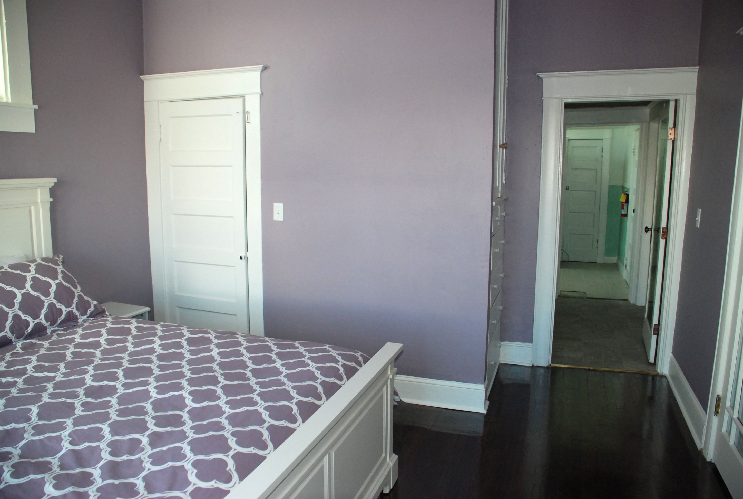 Un dormitorio con una cama, una puerta blanca y un pasillo que conduce a otra habitación.