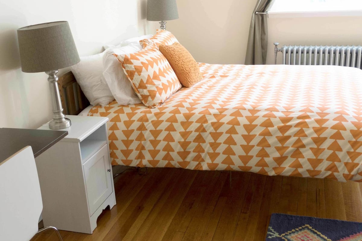 A bedroom with a bed, nightstands, a lamp, a window with curtains, and a patterned rug.