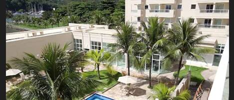 A hotel with a pool, palm trees, and a view of a mountain.
