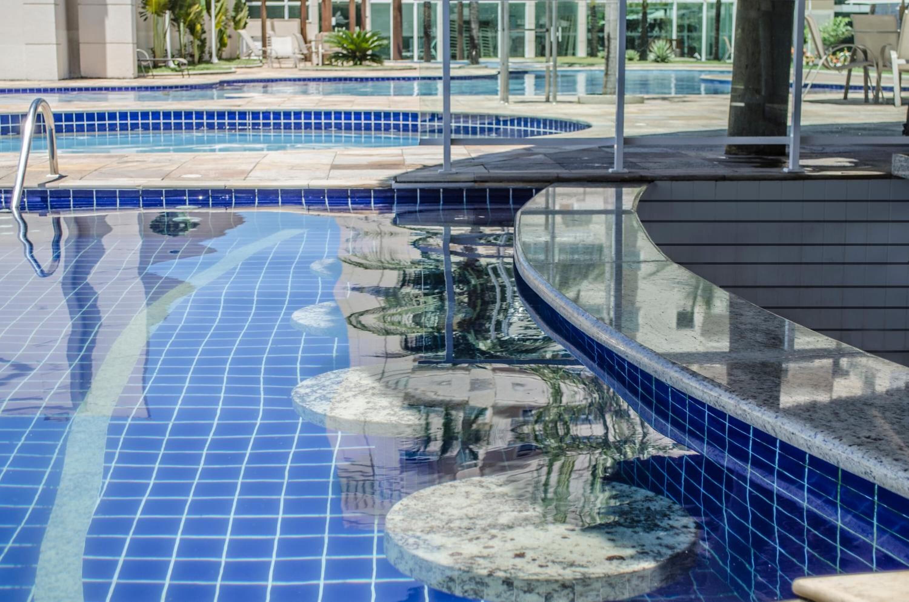 Una piscina con baldosas azules, una cubierta de madera y sillas de descanso.