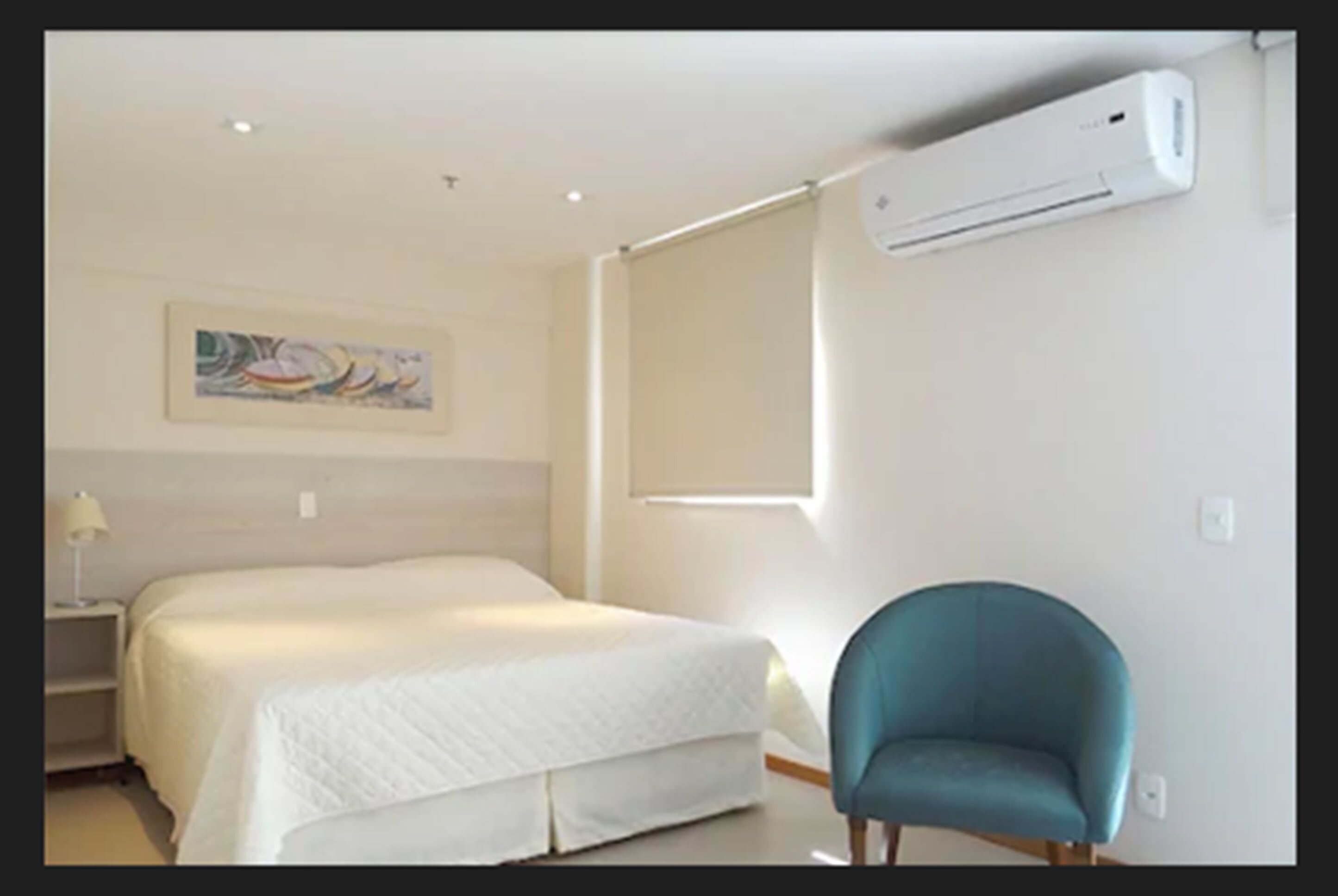 Una habitación de hotel con una cama, una silla, un equipo de aire acondicionado y una ventana.