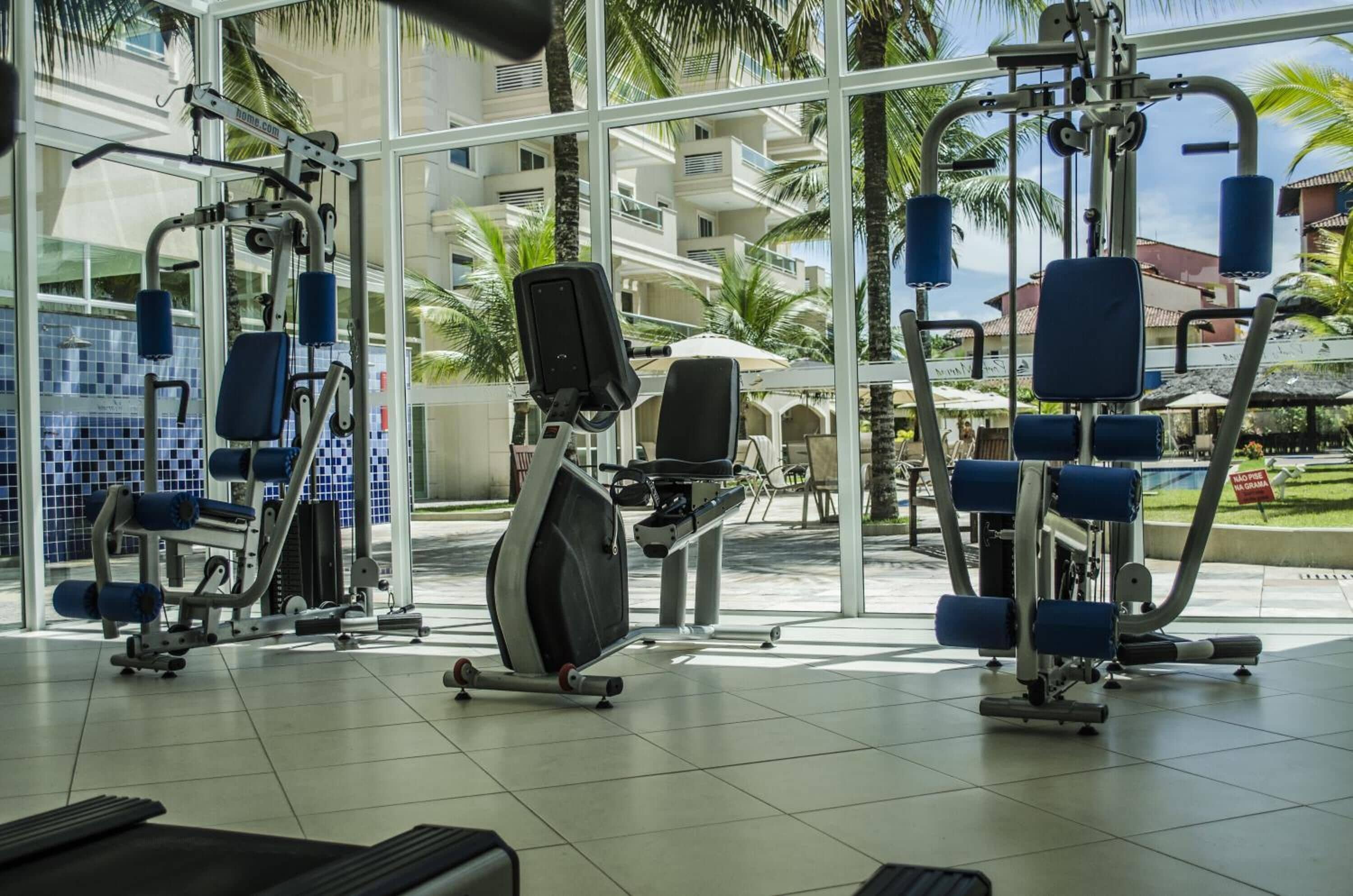 A gym with exercise equipment and a view of palm trees and a building in the background.