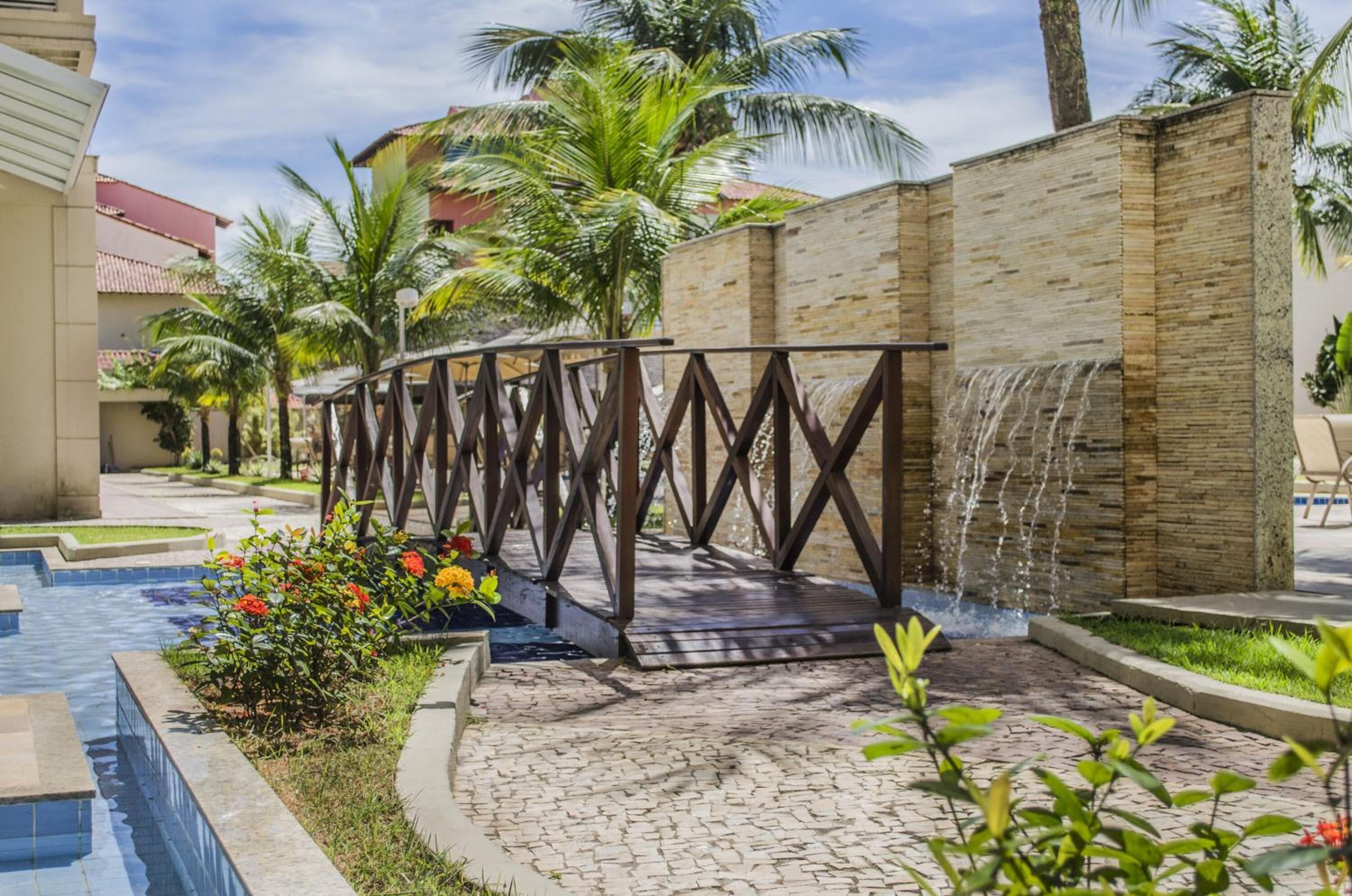 Un área de piscina con un puente de madera, palmeras y una cascada.
