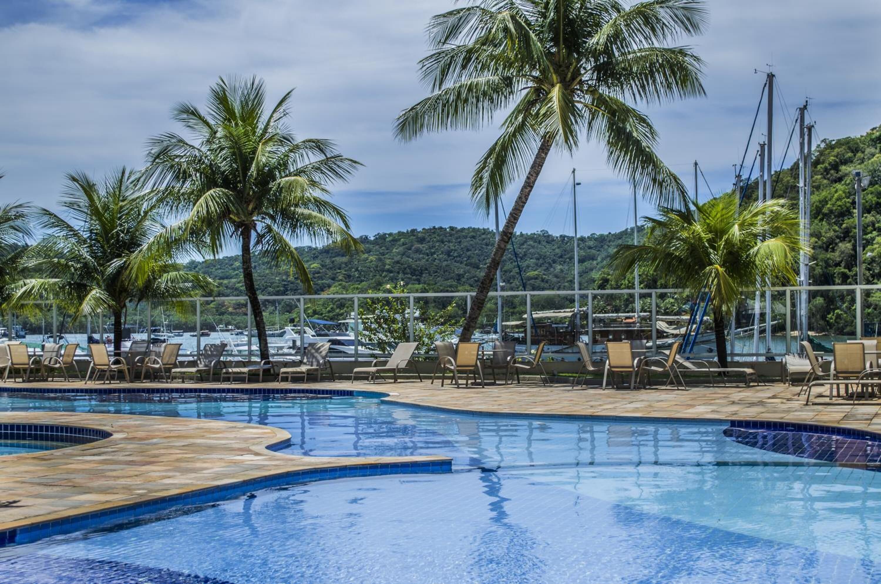 A pool area with lounge chairs and palm trees, surrounded by a fence and overlooking a marina.