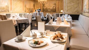Ein Essbereich mit gedeckten Tischen zum Frühstück, darunter Speisen, Tassen und eine Chandelier.