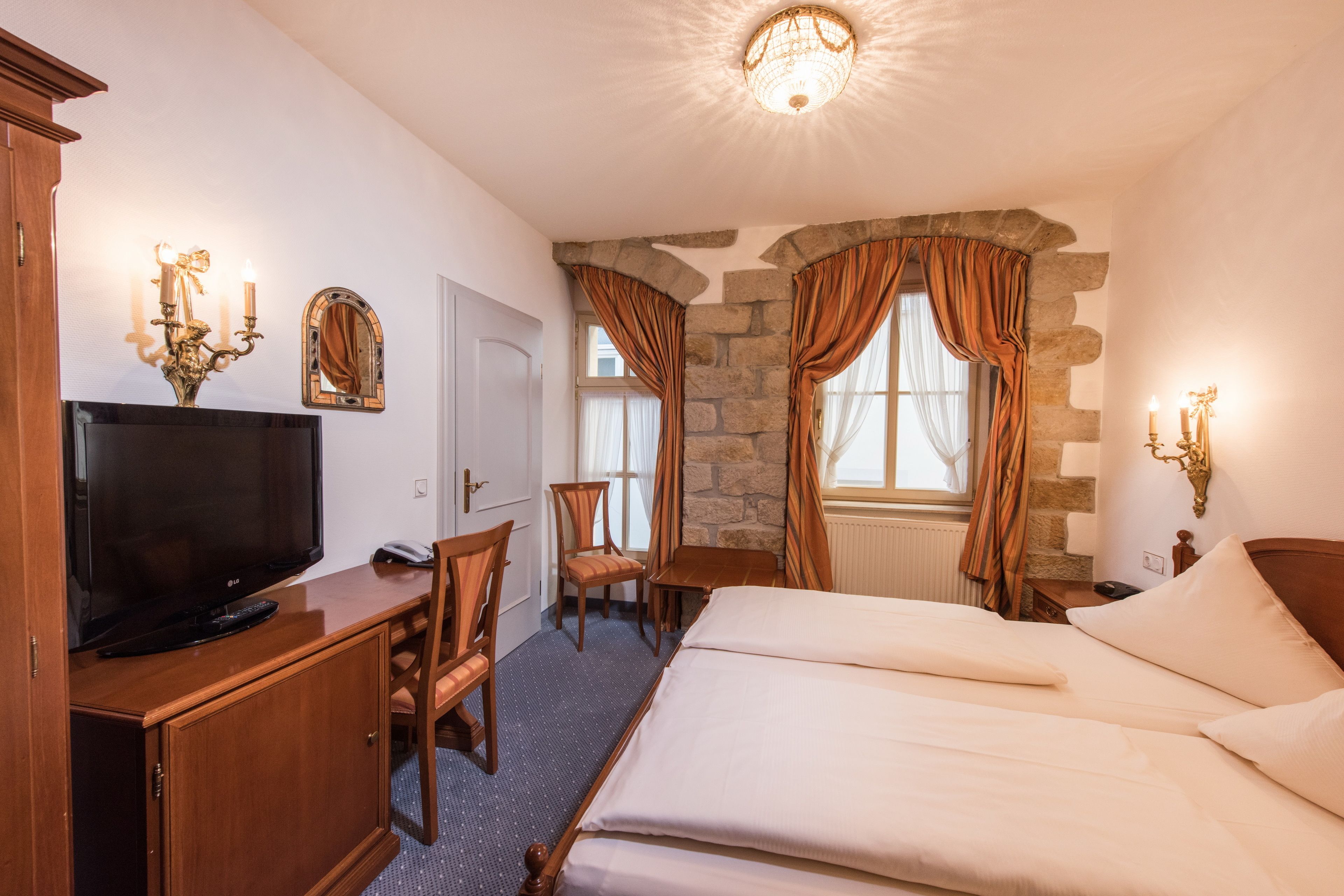 Ett hotellrum med en tv, trämöbler, en vägg av sten och en säng med vita sängkläder.