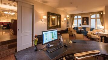 A hotel room with a desk, computer, and a seating area with a sofa and armchairs.