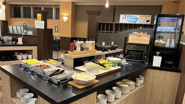 Zona de buffet amb diverses estacions de menjar, incloent una estació de pa i una altra de begudes.