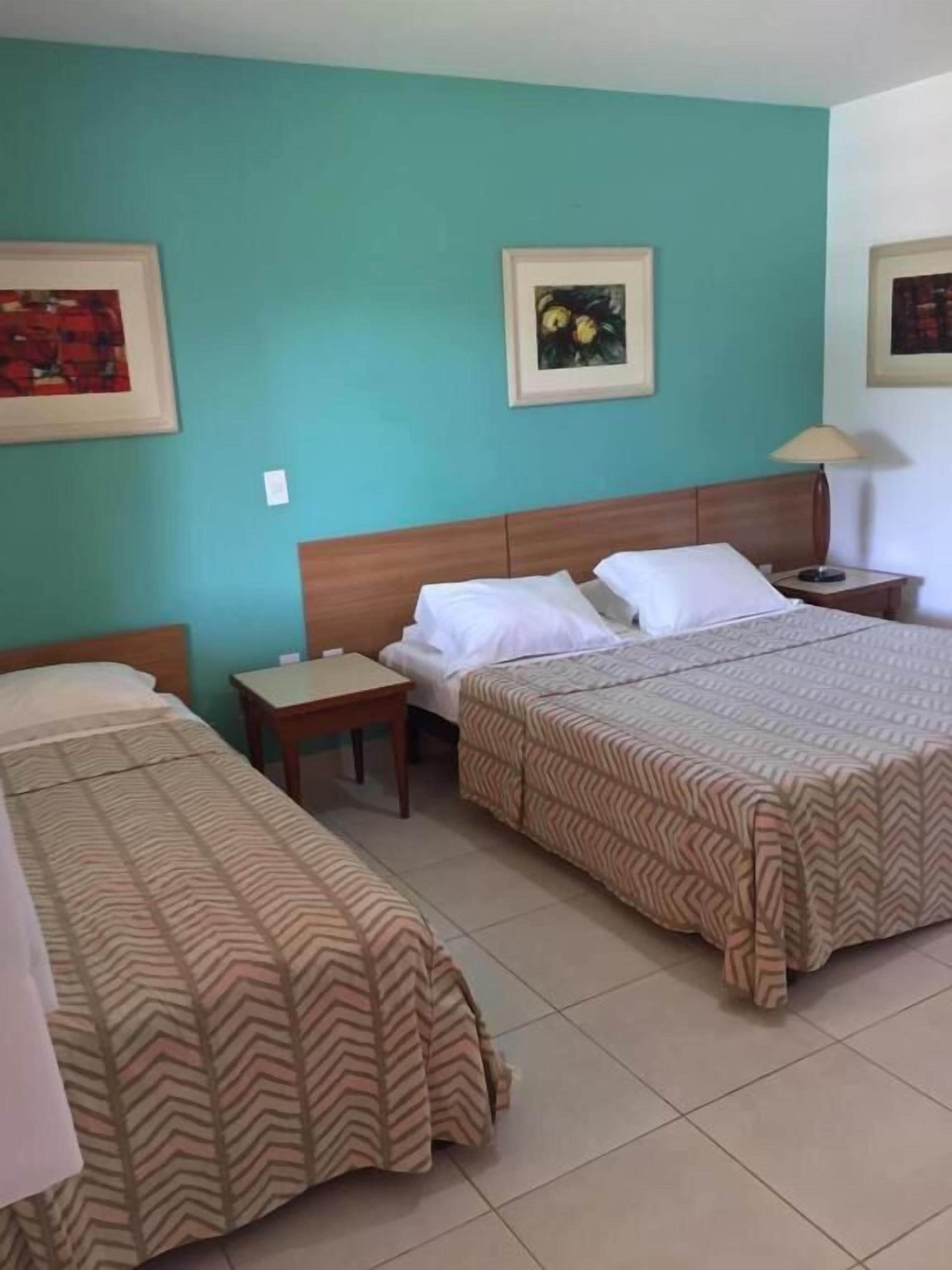 A hotel room with two beds, a wooden headboard, a nightstand, and a lamp.