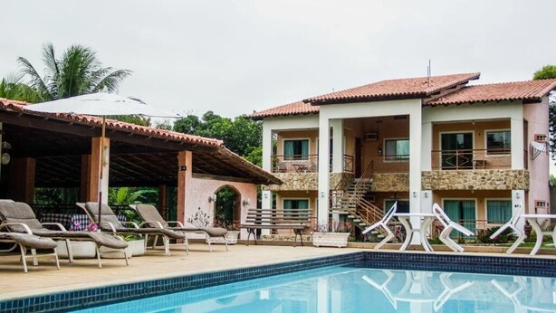 A poolside area with lounge chairs, a covered seating area, and a two-story building with balconies.