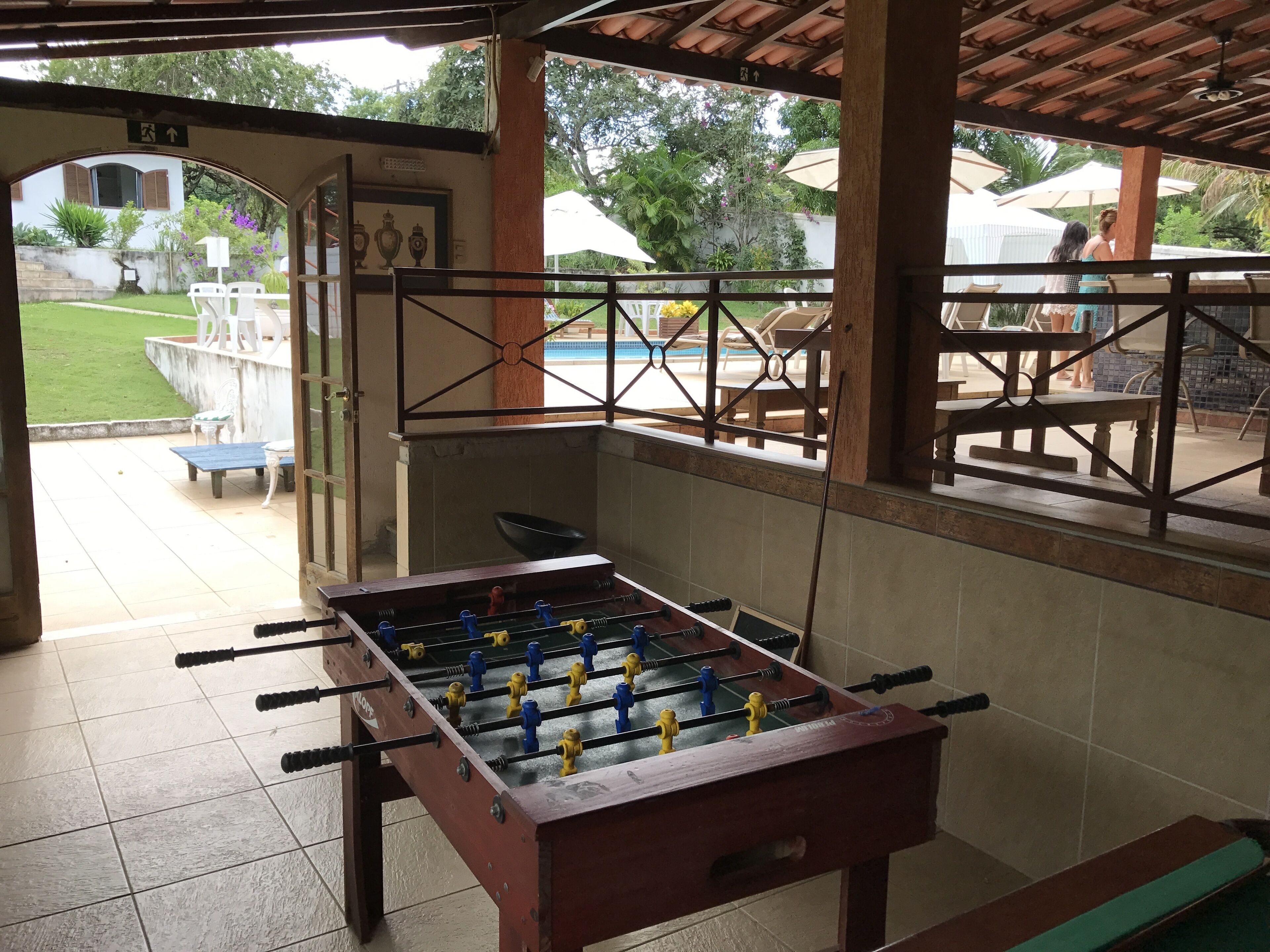 A foosball table in a covered outdoor area with a pool in the background.