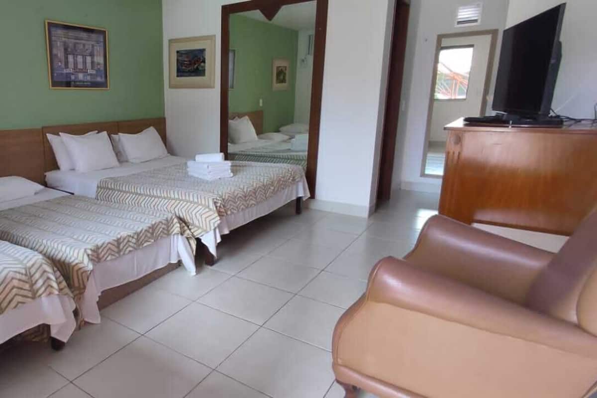 A hotel room with two beds, a wooden headboard, a TV, and a leather chair.