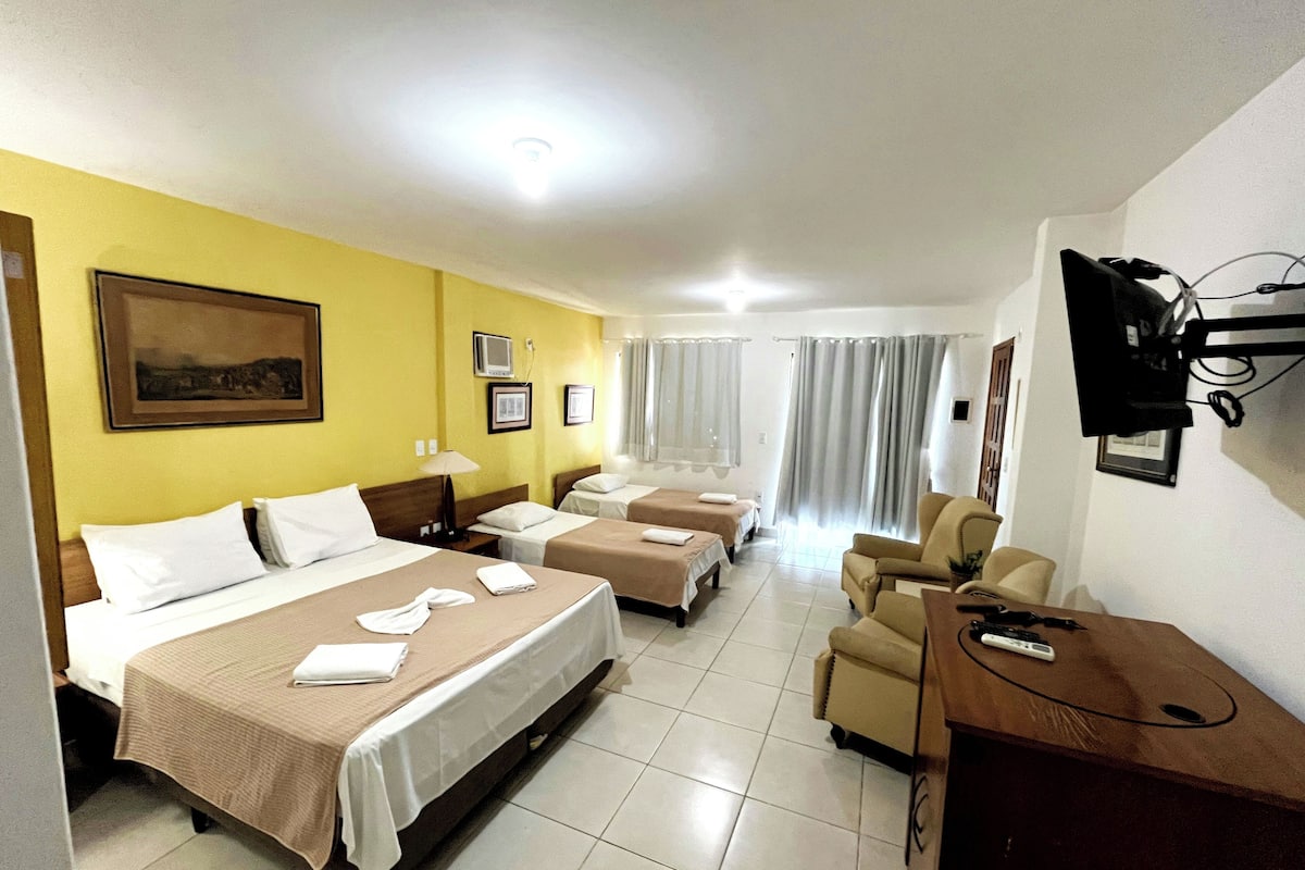 A hotel room with two beds, a desk, a chair, a TV, and a window with curtains.