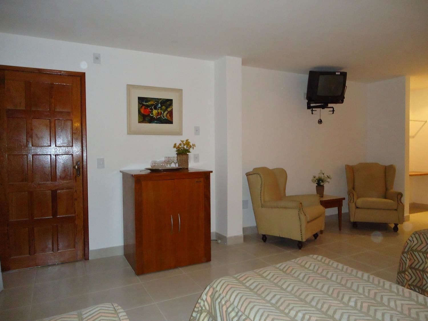 A living room with a wooden cabinet, two armchairs, a television mounted on the wall, and a framed picture on the wall.