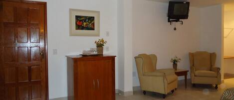 A living room with a wooden cabinet, two armchairs, a television mounted on the wall, and a framed picture on the wall.