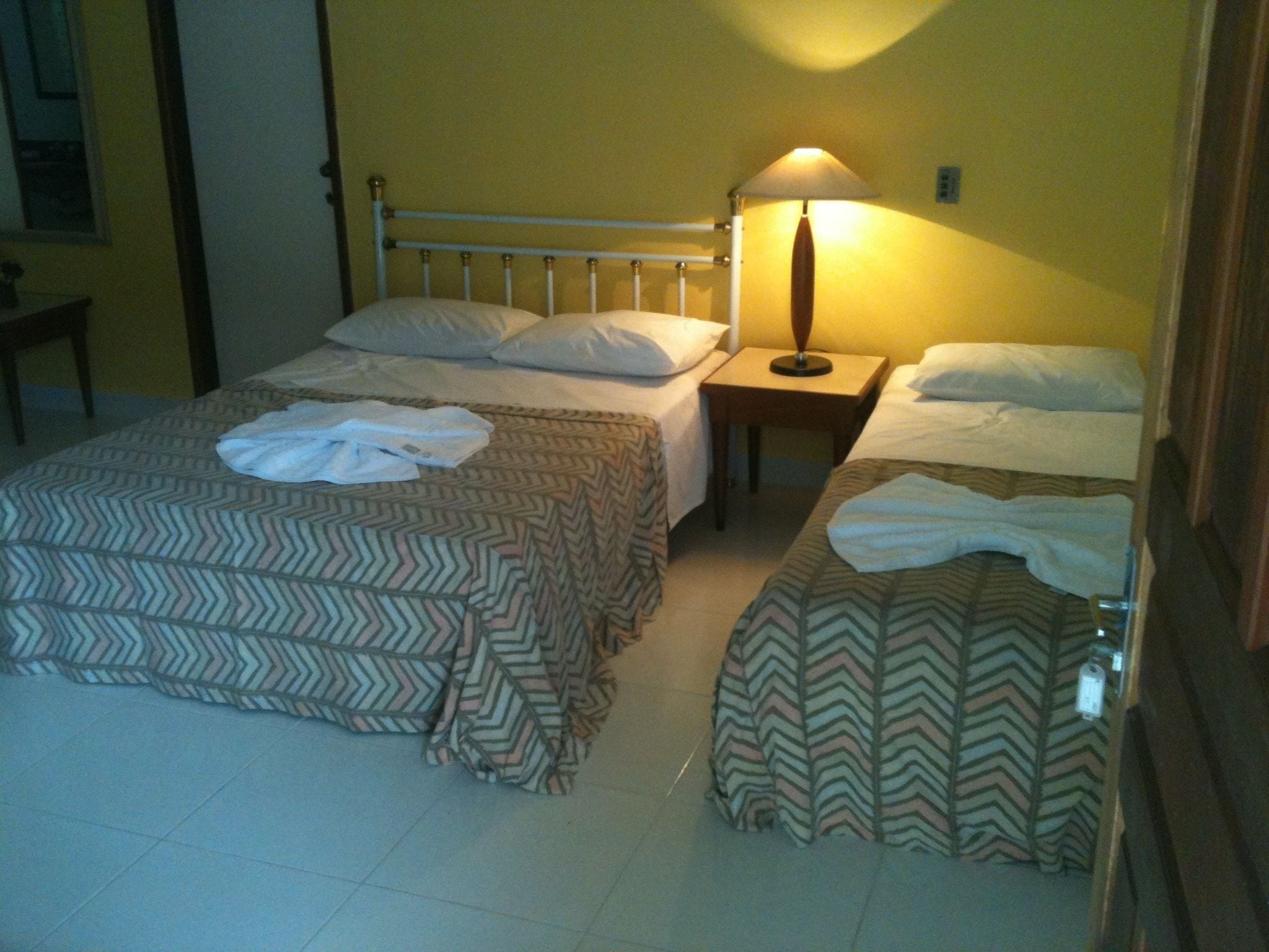 Une chambre avec deux lits, chacun recouvert d’une couvre-lit à motifs et agrémenté d’oreillers. Une table de chevet avec une lampe se trouve sur l’un des côtés.
