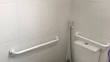 A small, white-tiled bathroom with a toilet, a handrail, and a grab bar.