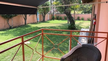 A balcony with a wicker chair, a metal railing, and a view of a well-maintained lawn and trees.