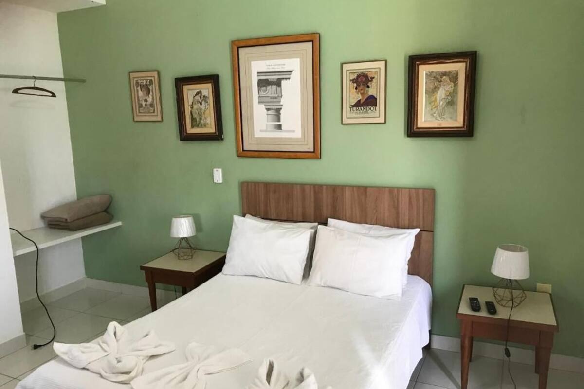 A hotel room with a large bed, two bedside tables, a hanging light, and framed pictures on the wall.