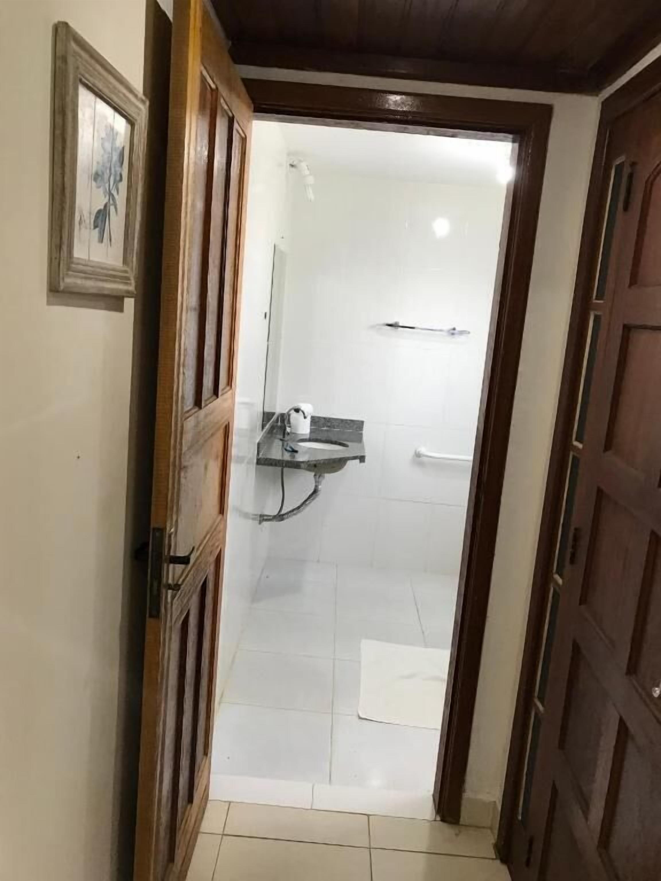Casa de banho com azulejos brancos, chuveiro e um pequeno armário com produtos de higiene pessoal.