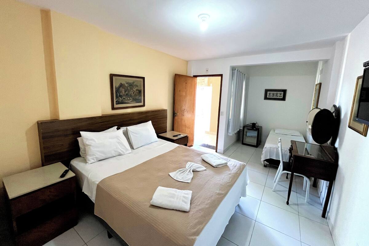 A hotel room with a bed, bedside table, nightstand, and a desk with a chair.