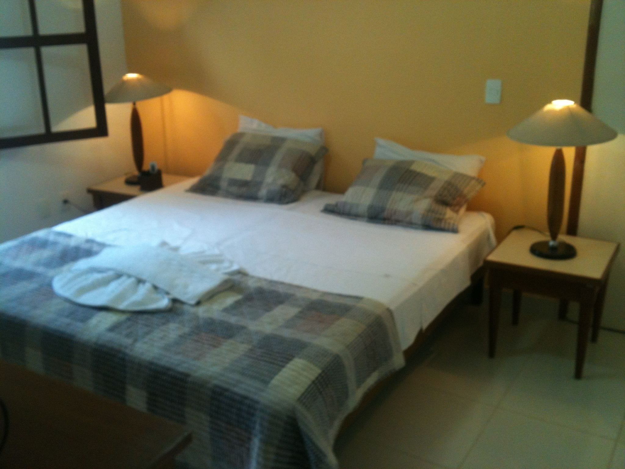 A neatly made bed with a checkered bedspread and pillows, two bedside lamps, and a small table with a lamp.