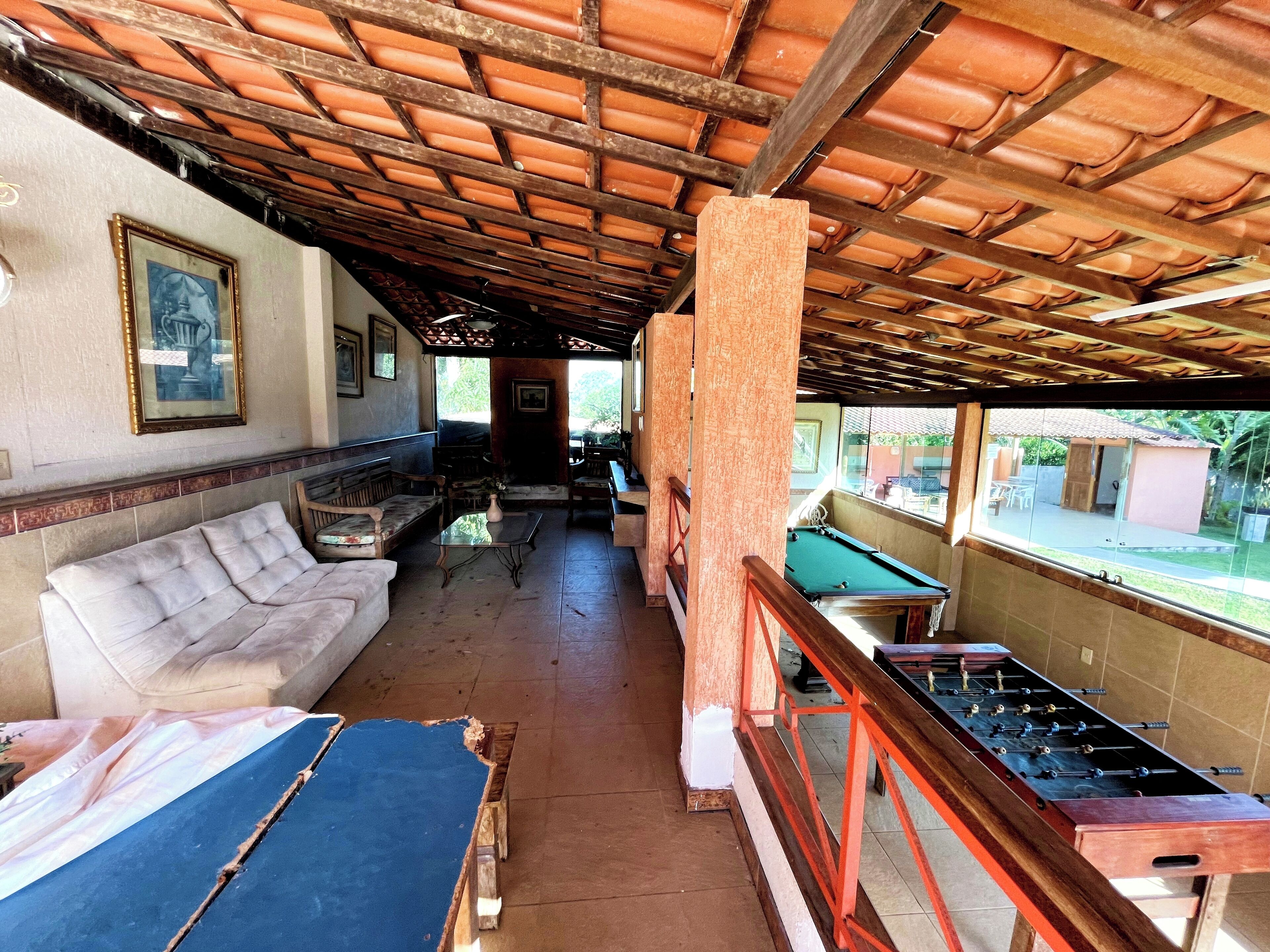 A covered outdoor seating area with a pool table, sofas, and a foosball table.