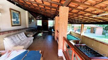 A covered outdoor seating area with a pool table, sofas, and a foosball table.